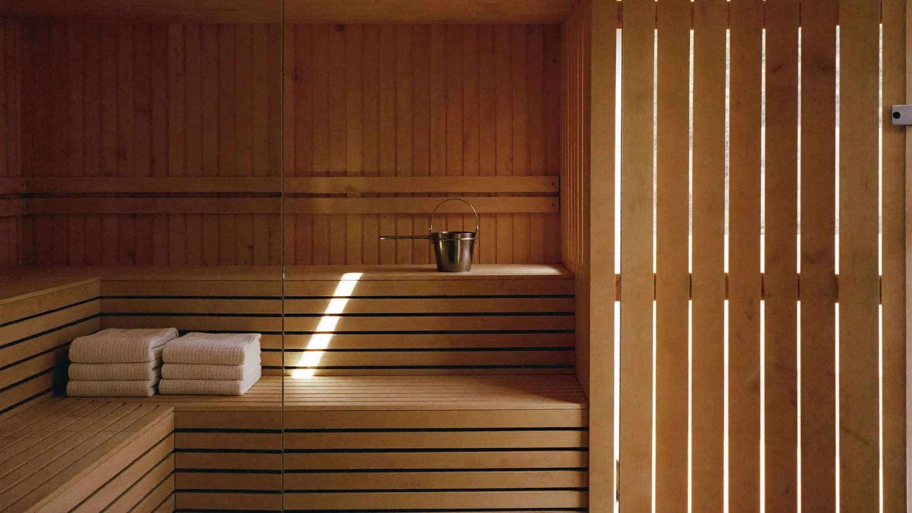Sauna mit hellen Holzbänken, gefalteten weißen Handtüchern und einem Streifen Tageslicht